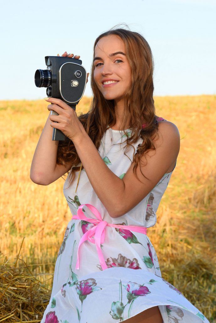 Голая девушка в поле с ретро видеокамерой.